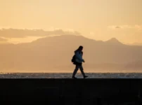 夕暮れの水辺を一人の人物が静かに歩く情景｜懐かしい情景が静かによみがえる、やさしい記憶のイメージ写真