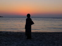 夕暮れの海辺で女性が静かに佇む後ろ姿の風景｜懐かしい情景が静かによみがえる、やさしい記憶のイメージ写真