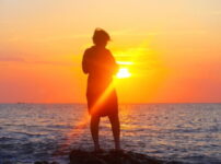 夕暮れの海辺に佇む女性のシルエット｜懐かしい情景が静かによみがえる、やさしい記憶のイメージ写真