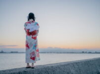 夕暮れの海辺で女性が静かに佇む情景｜懐かしい情景が静かによみがえる、やさしい記憶のイメージ写真
