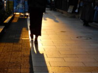 夕暮れの都会を歩く女性の後ろ姿と長く伸びる影が印象的な風景｜懐かしい情景が静かによみがえる、やさしい記憶のイメージ写真