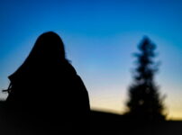 夕暮れの空を背景に、女性のシルエットが静かに佇む情景｜懐かしい情景が静かによみがえる、やさしい記憶のイメージ写真