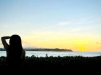 夕暮れの海を前に、女性が静かに佇む後ろ姿の情景｜懐かしい情景が静かによみがえる、やさしい記憶のイメージ写真