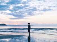 夕暮れの海辺で女性が静かに佇む情景｜懐かしい情景が静かによみがえる、やさしい記憶のイメージ写真