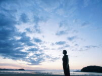 夕暮れの海辺で女性が静かに佇む情景｜懐かしい情景が静かによみがえる、やさしい記憶のイメージ写真