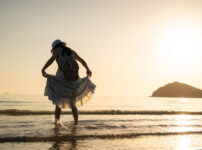夕暮れの海辺で、女性が静かに佇みながら柔らかな光に包まれている情景｜懐かしい情景が静かによみがえる、やさしい記憶のイメージ写真