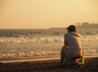 夕暮れの海辺で女性が静かに海を見つめる情景｜懐かしい情景が静かによみがえる、やさしい記憶のイメージ写真