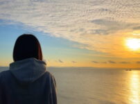 夕暮れの海辺で女性が静かに佇む情景｜懐かしい情景が静かによみがえる、やさしい記憶のイメージ写真